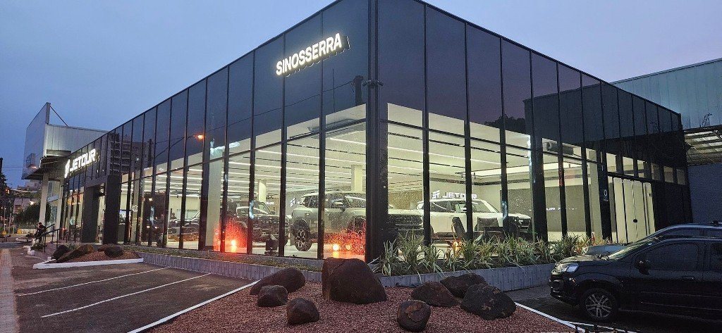 Fachada iluminada de uma concessionária do Grupo Sinosserra ao entardecer